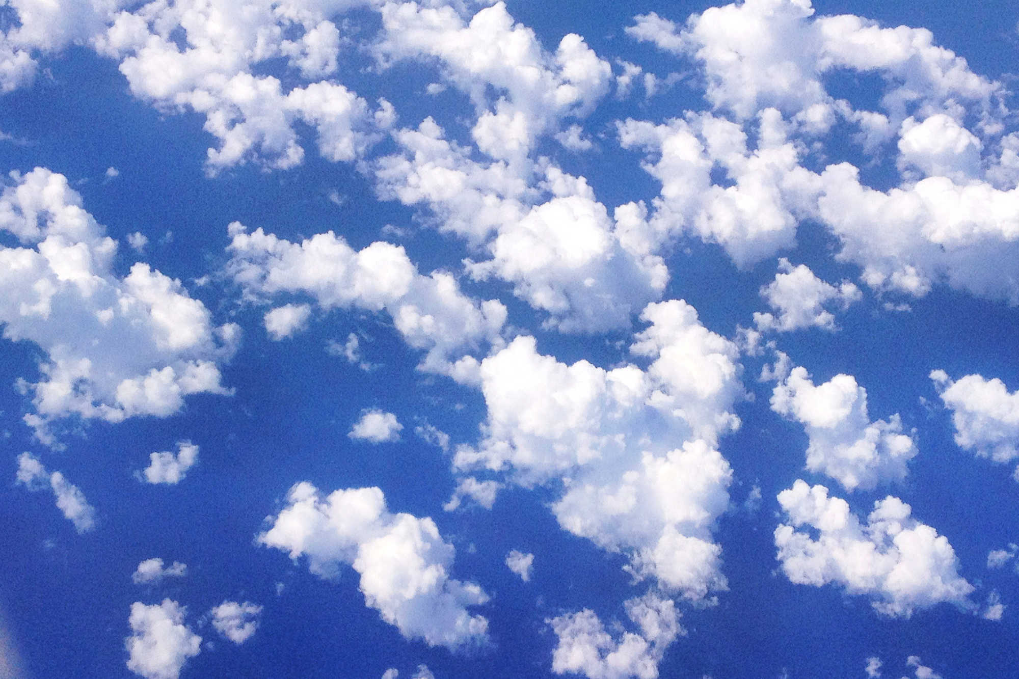 Blue sky and white puffy clouds from an airplane window