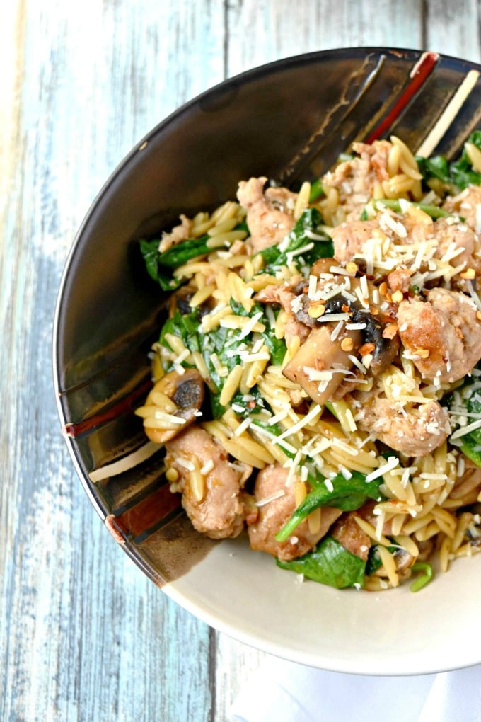 One Pot Italian Sausage Orzo with Spinach and mushrooms garnished with Parmesan cheese and crushed red peppers.