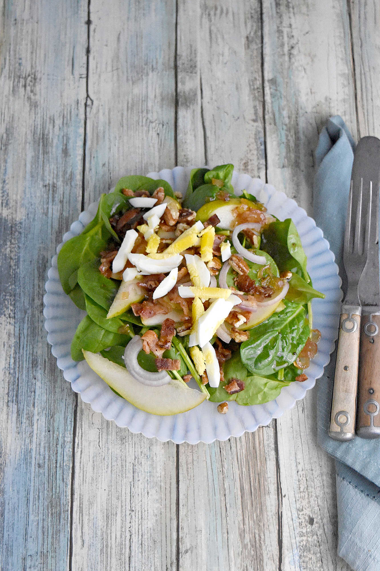 Sweet and tangy bacon dressing is drizzled over sweet pears, spinach, and sliced shallots. Top Wilted Pear and Shallot Salad with chopped pecans and sliced hard-boiled eggs for a hearty and delicious salad. #wiltedsalad #spinachsalad #pearsalad #bacondressing #WiltedSaladSensation #PearShallotEats #FarmtoTableFaves #HealthyGreensInspo #BlissfulBitesByUs