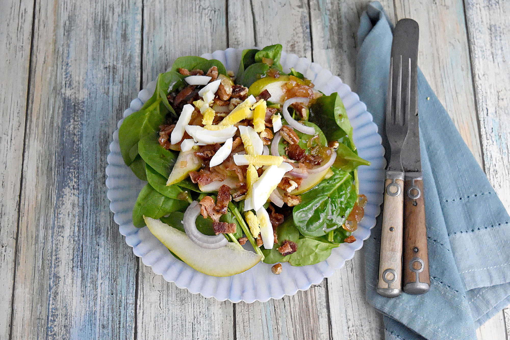 Sweet and tangy bacon dressing is drizzled over sweet pears, spinach, and sliced shallots. Top Wilted Pear and Shallot Salad with chopped pecans and sliced hard-boiled eggs for a hearty and delicious salad. #wiltedsalad #spinachsalad #pearsalad #bacondressing #WiltedSaladSensation #PearShallotEats #FarmtoTableFaves #HealthyGreensInspo #BlissfulBitesByUs