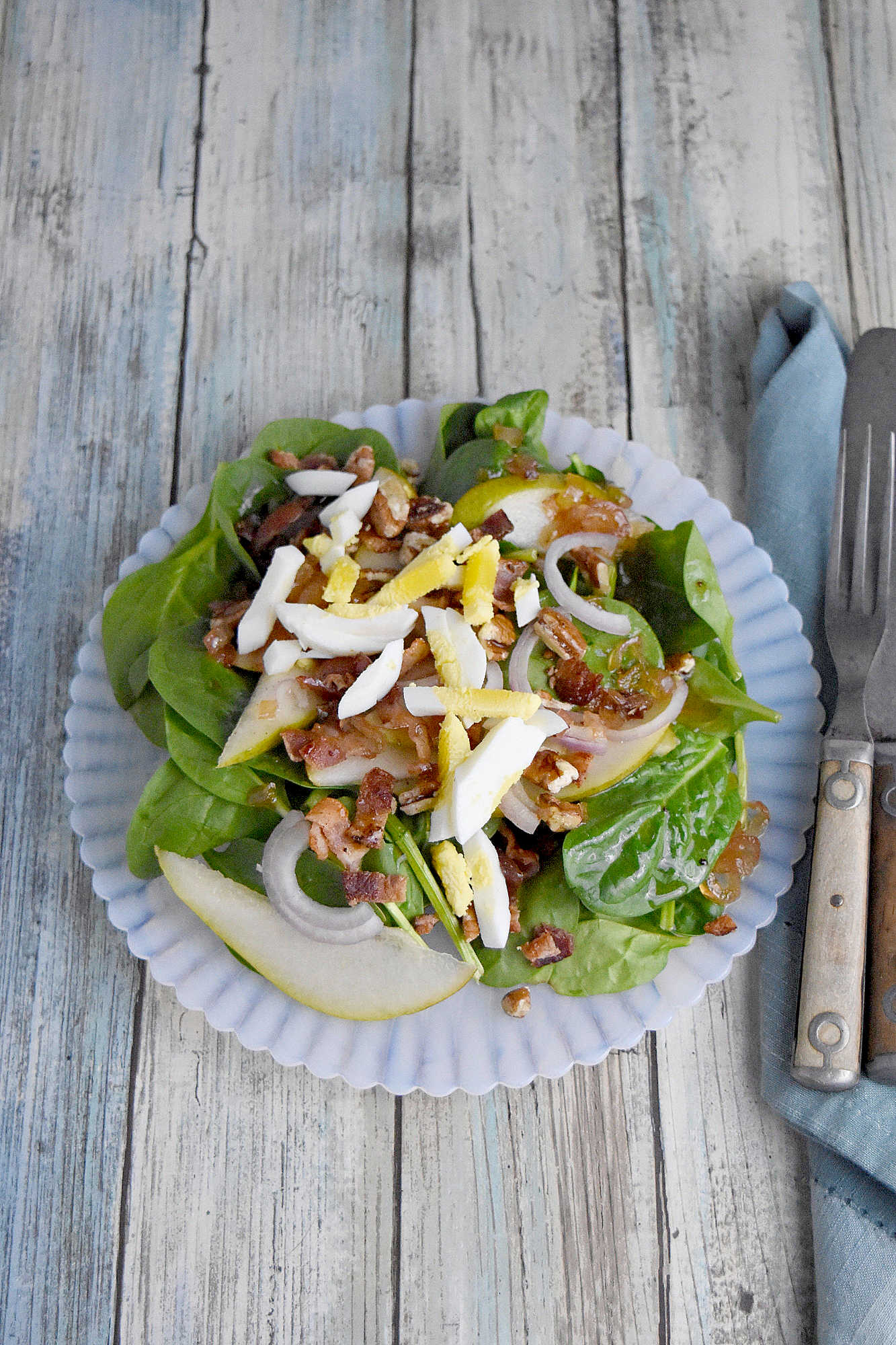 Sweet and tangy bacon dressing is drizzled over sweet pears, spinach, and sliced shallots. Top Wilted Pear and Shallot Salad with chopped pecans and sliced hard-boiled eggs for a hearty and delicious salad. #wiltedsalad #spinachsalad #pearsalad #bacondressing #WiltedSaladSensation #PearShallotEats #FarmtoTableFaves #HealthyGreensInspo #BlissfulBitesByUs