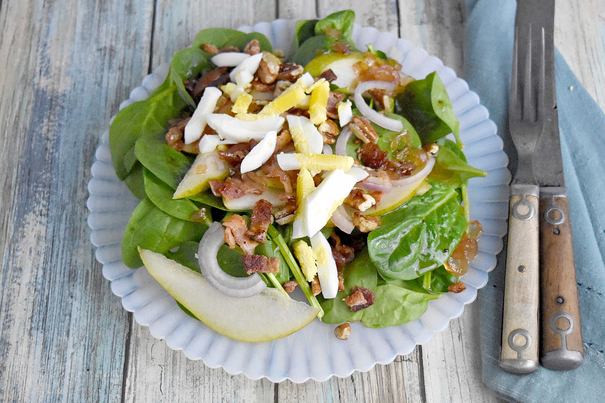 Sweet and tangy bacon dressing is drizzled over sweet pears, spinach, and sliced shallots. Top Wilted Pear and Shallot Salad with chopped pecans and sliced hard-boiled eggs for a hearty and delicious salad. #wiltedsalad #spinachsalad #pearsalad #bacondressing #WiltedSaladSensation #PearShallotEats #FarmtoTableFaves #HealthyGreensInspo #BlissfulBitesByUs