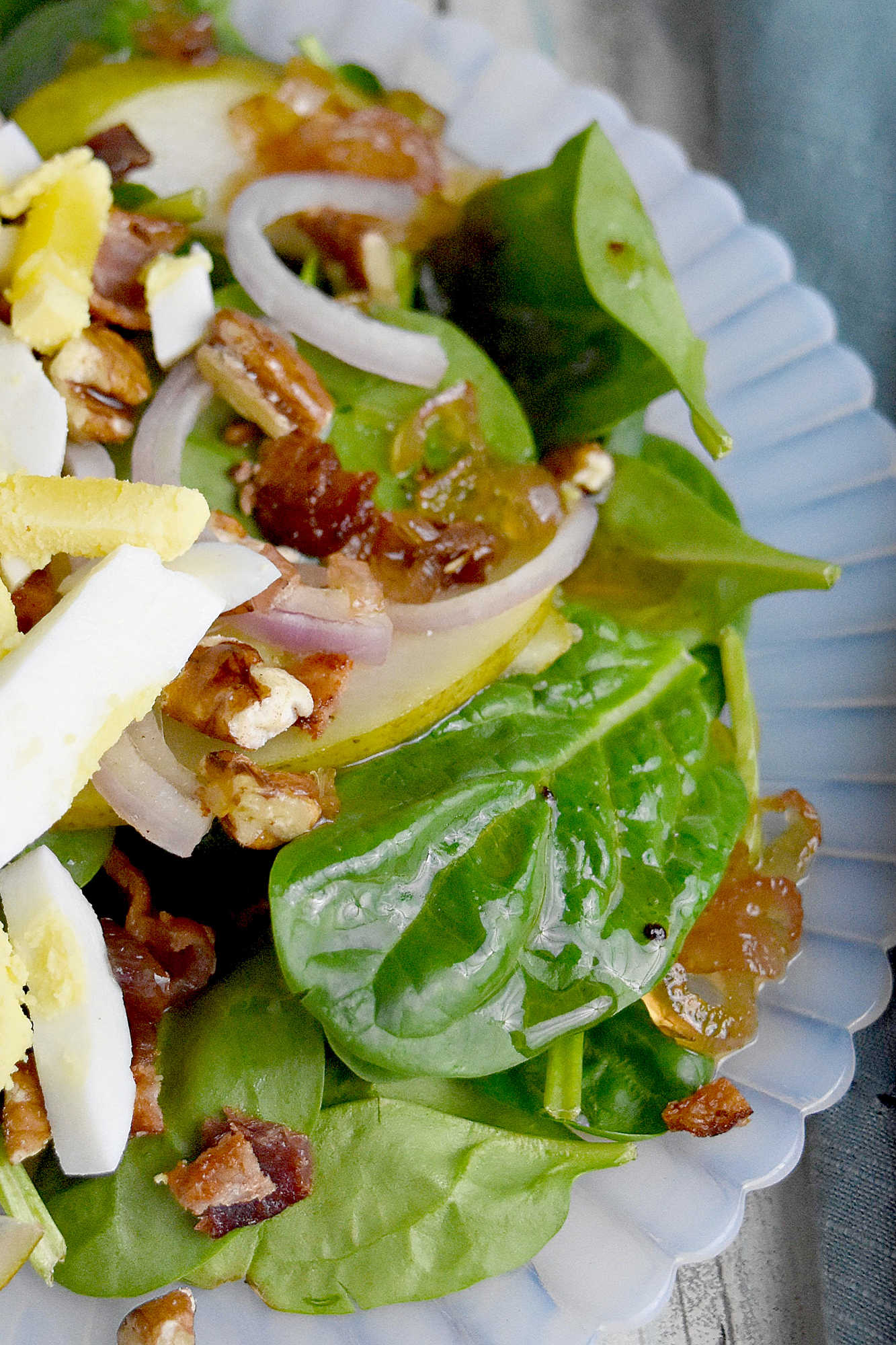 Sweet and tangy bacon dressing is drizzled over sweet pears, spinach, and sliced shallots. Top Wilted Pear and Shallot Salad with chopped pecans and sliced hard-boiled eggs for a hearty and delicious salad. #wiltedsalad #spinachsalad #pearsalad #bacondressing #WiltedSaladSensation #PearShallotEats #FarmtoTableFaves #HealthyGreensInspo #BlissfulBitesByUs