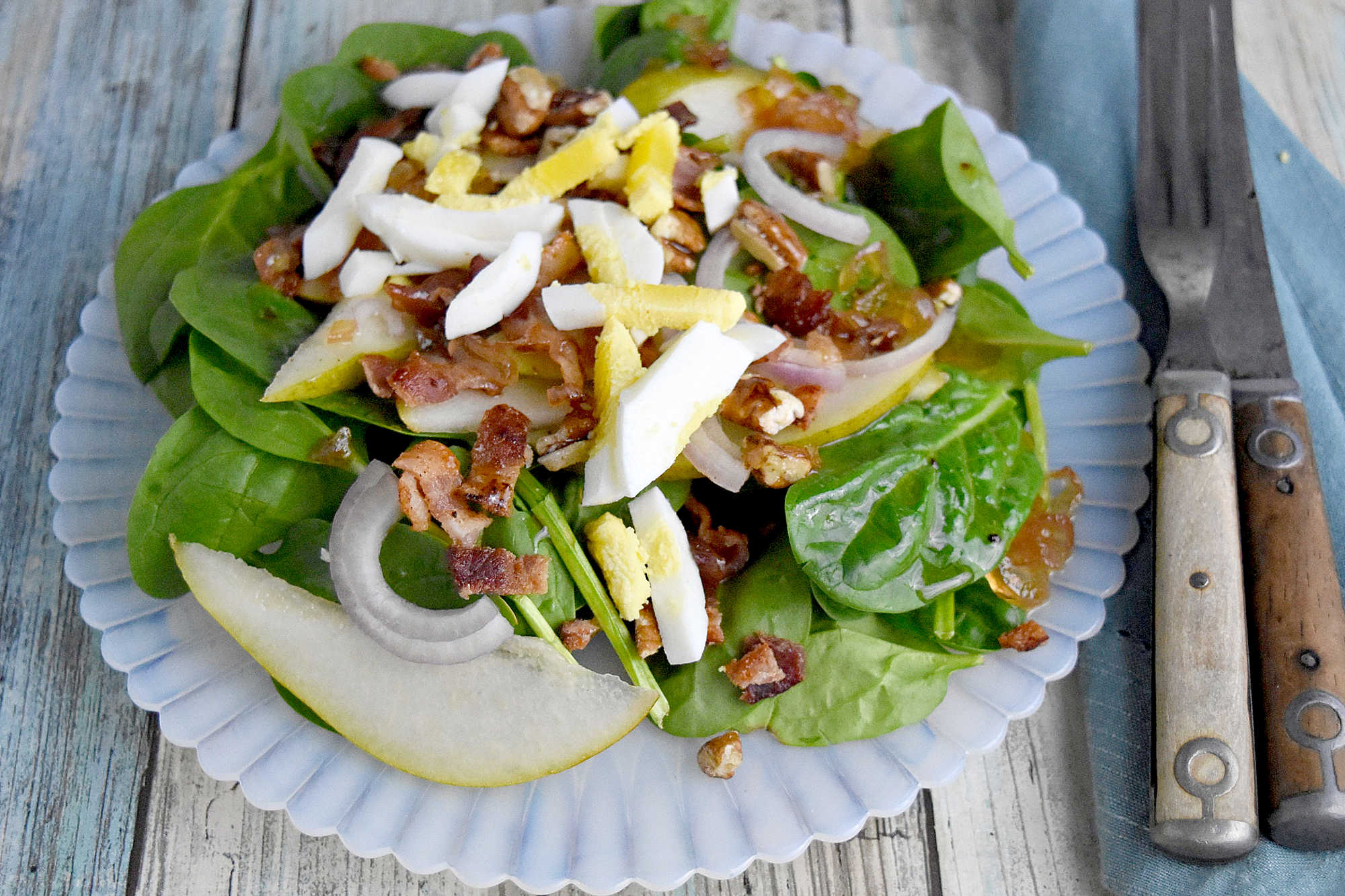 Sweet and tangy bacon dressing is drizzled over sweet pears, spinach, and sliced shallots. Top Wilted Pear and Shallot Salad with chopped pecans and sliced hard-boiled eggs for a hearty and delicious salad. #wiltedsalad #spinachsalad #pearsalad #bacondressing #WiltedSaladSensation #PearShallotEats #FarmtoTableFaves #HealthyGreensInspo #BlissfulBitesByUs