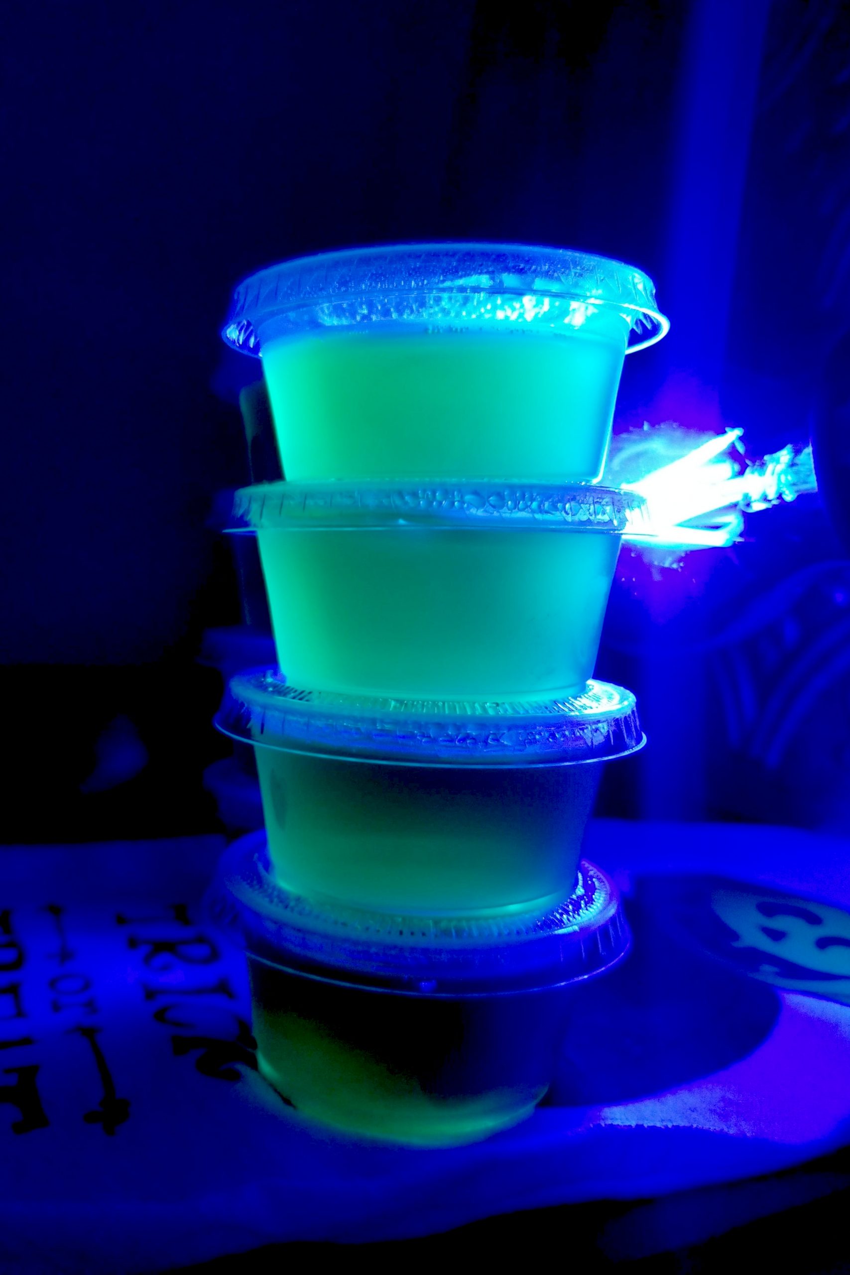 Radioactive Jell-O Shots are a simple gin and tonic with lime Jell-O.  The tonic water makes them glow under a black light which makes them even more fun to eat! #HalloweenTreatsWeek