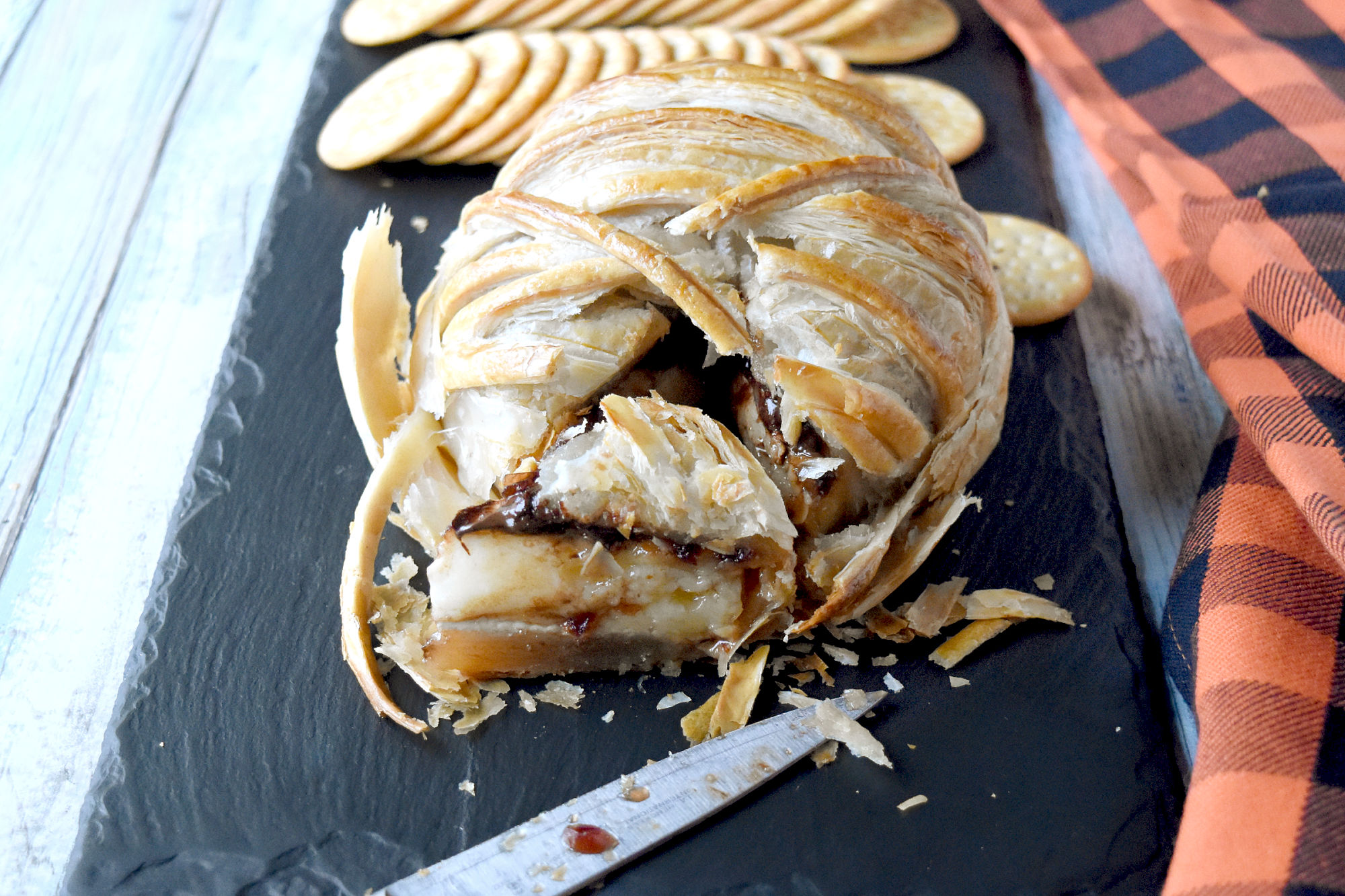 Oozing Mummy Baked Brie is topped with dried cranberries simmered in orange juice and dark chocolate chips.  It’s a sweet and savory treat for an appetizer or dessert and super simple to make. #HalloweenTreatsWeek #bakedbrie