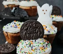 Fluffy white cupcakes have crushed cookies folded into the batter and a whole cookie hidden at the bottom. They’re topped with creamy frosting, colorful Halloween sprinkles, and Peeps ghosts.
