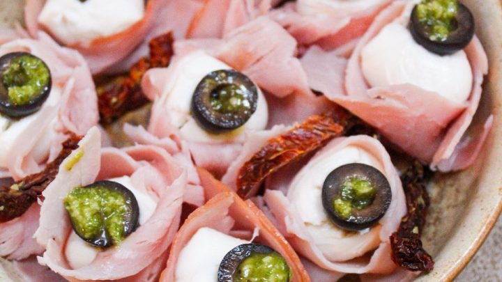 Antipasto Eyeballs made with fresh mozzarella wrapped in ham, topped with olives, and finished with pesto and sundried tomatoes.