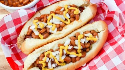 Franks-N-Beans Hot Dog is not your average hot dog. Wrapped in bacon, grilled, topped with beans, onion, and mustard make a new favorite to your summer BBQ.