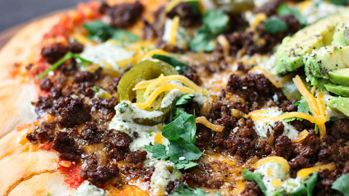 Learn how to make Taco Pizza with seasoned ground beef, refried beans, melted cheese, and all your favorite fresh taco toppings. An easy family dinner!